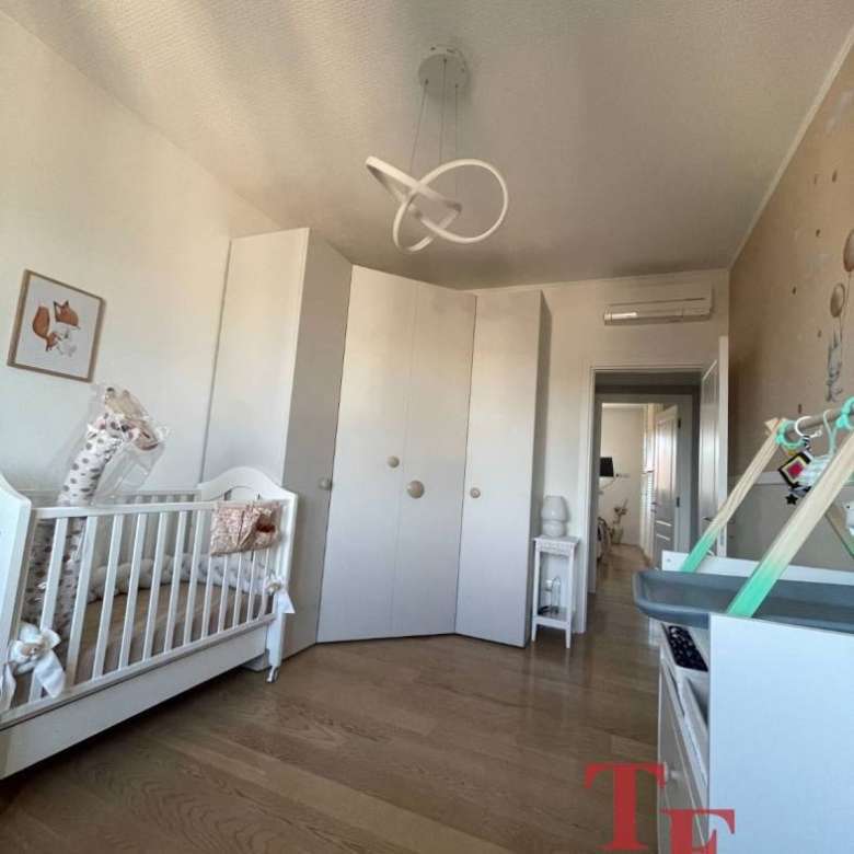 Красивая детская комната с белой мебелью, деревянным полом и современной люстрой в светлых тонах, идеально подходящая для малыша.