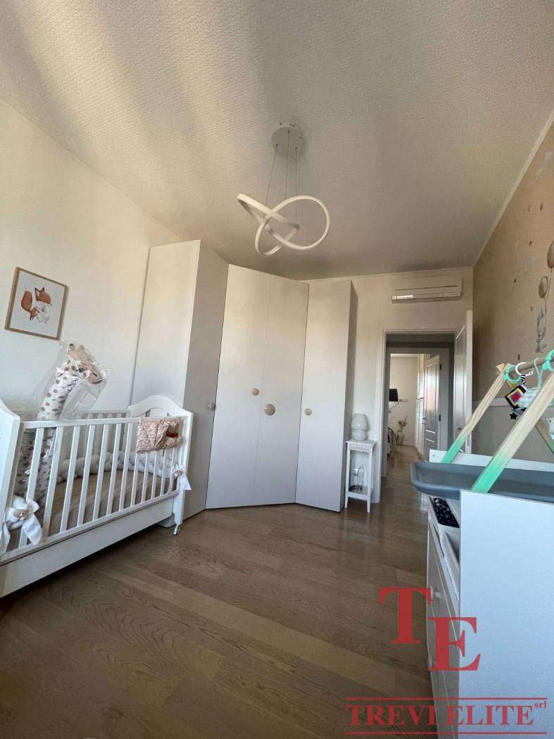 Красивая детская комната с белой мебелью, деревянным полом и современной люстрой в светлых тонах, идеально подходящая для малыша.