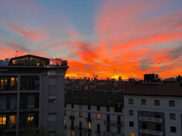 Эксклюзивный вид на городские здания на фоне живописного заката с яркими красными и оранжевыми оттенками неба.