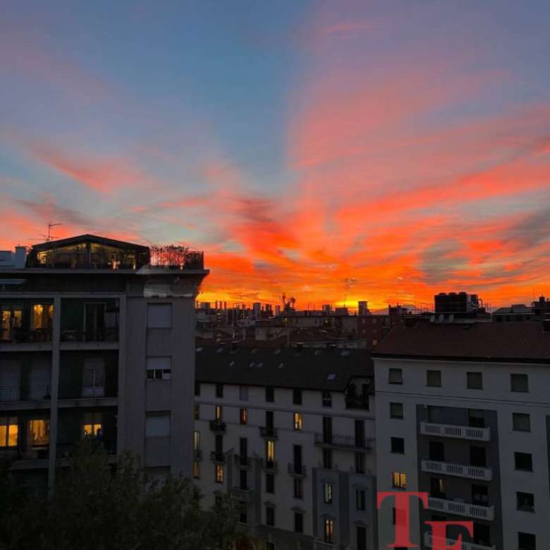 Эксклюзивный вид на городские здания на фоне живописного заката с яркими красными и оранжевыми оттенками неба.