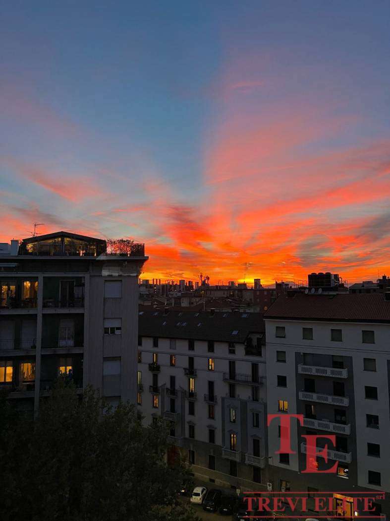 Эксклюзивный вид на городские здания на фоне живописного заката с яркими красными и оранжевыми оттенками неба.