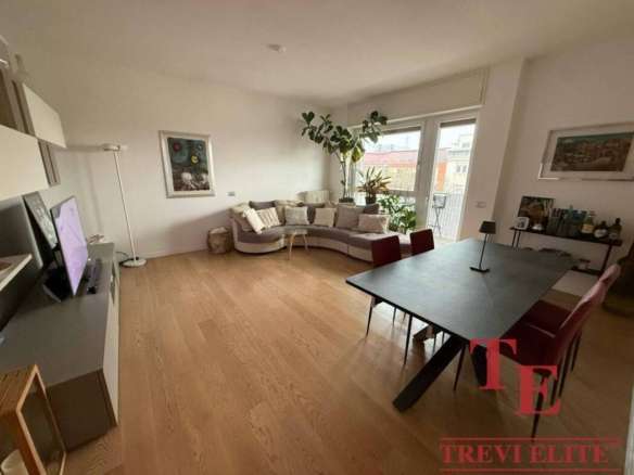 Элегантная гостиная с просторным диваном, большим окном и зелеными растениями высокого роста, ярким освещением и современной мебелью, создающая комфорт и уют в высококлассной недвижимости.