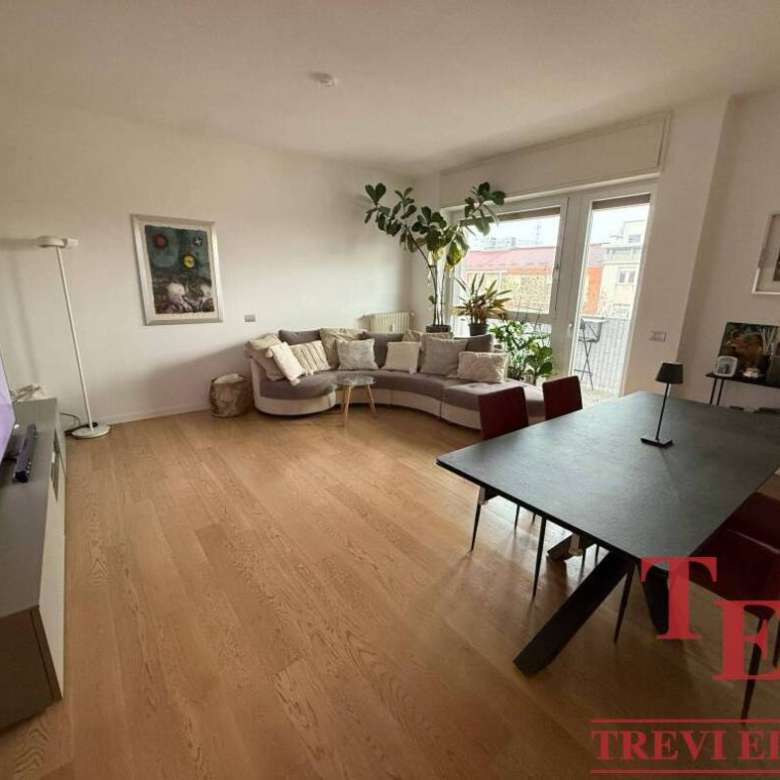 Элегантная гостиная с просторным диваном, большим окном и зелеными растениями высокого роста, ярким освещением и современной мебелью, создающая комфорт и уют в высококлассной недвижимости.