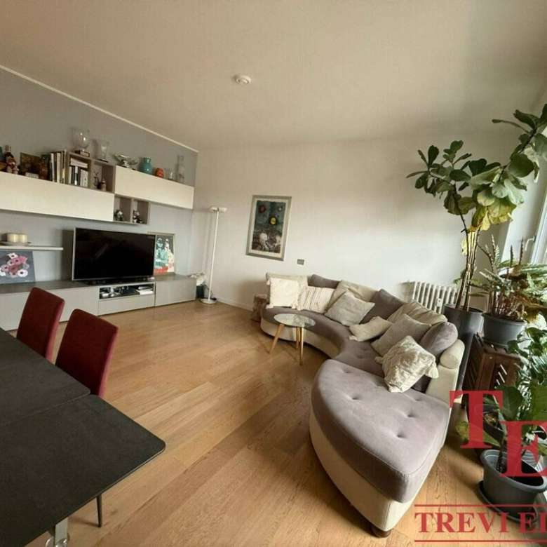 Уютная гостиная с большими окнами и зелеными растениями, современная мебель и стильный дизайн, идеально подходит для элитных апартаментов с видом на город.