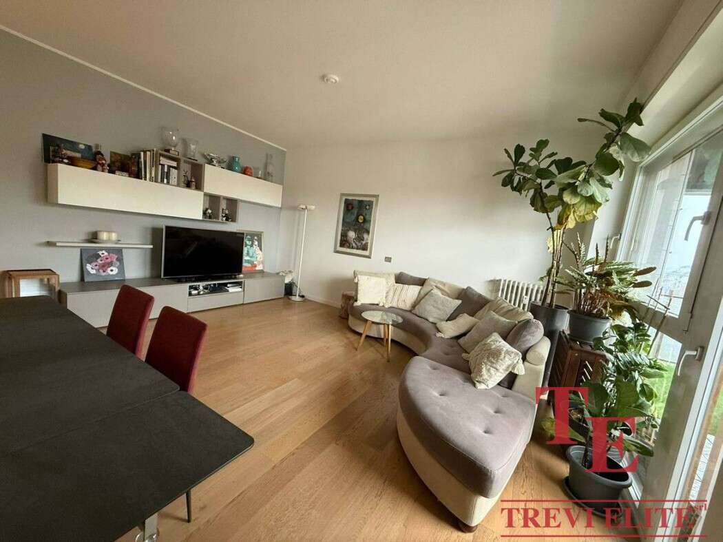 Уютная гостиная с большими окнами и зелеными растениями, современная мебель и стильный дизайн, идеально подходит для элитных апартаментов с видом на город.