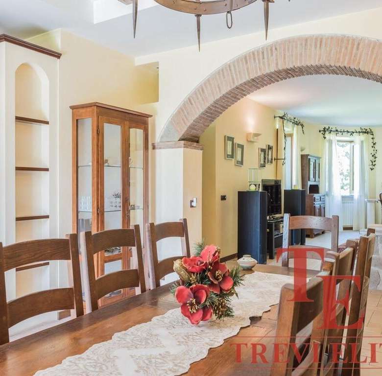 Современный интерьер уютного дома с деревянной мебелью, цветами и каменной отделкой, часть кухни и гостиной, светлые стены и большие окна.