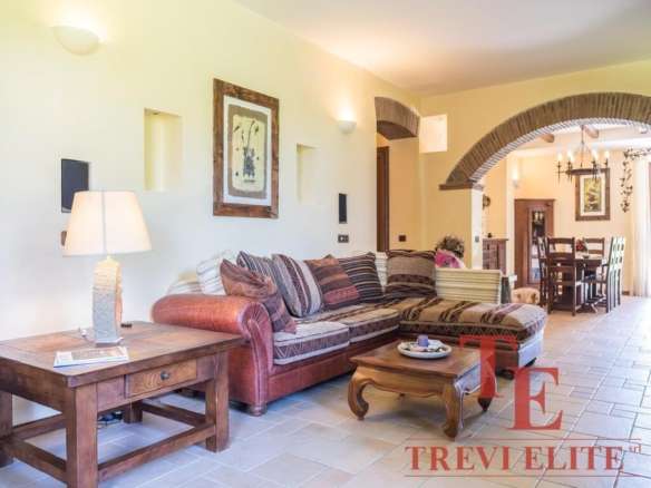 Уютная гостиная в стиле тосканского дома с деревянной мебелью и мягким диваном, светло-желтые стены, арочный проём и теплое освещение создают атмосферу комфорта и уюта.