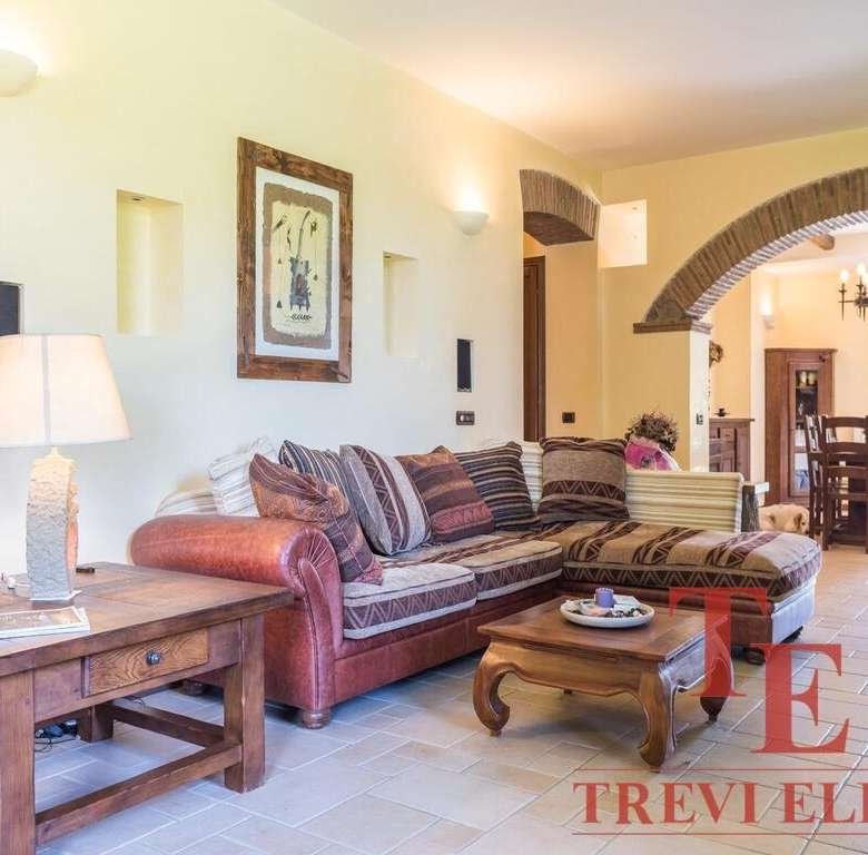 Уютная гостиная в стиле тосканского дома с деревянной мебелью и мягким диваном, светло-желтые стены, арочный проём и теплое освещение создают атмосферу комфорта и уюта.