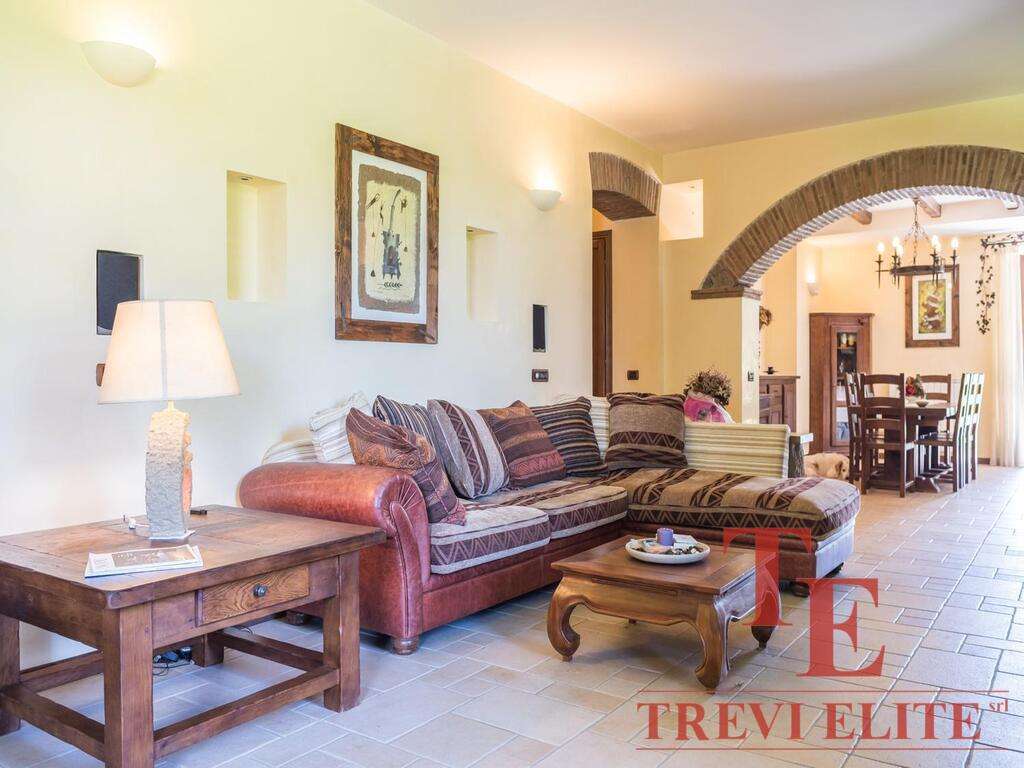 Уютная гостиная в стиле тосканского дома с деревянной мебелью и мягким диваном, светло-желтые стены, арочный проём и теплое освещение создают атмосферу комфорта и уюта.