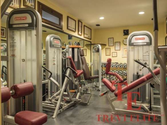 Снимок тренажерного зала с современным оборудованием и красными креслами для занятий фитнесом. Идеальное пространство для занятий спортом и поддержания формы. Агентство недвижимости Треви Элит.