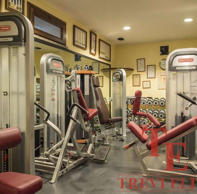 Снимок тренажерного зала с современным оборудованием и красными креслами для занятий фитнесом. Идеальное пространство для занятий спортом и поддержания формы. Агентство недвижимости Треви Элит.