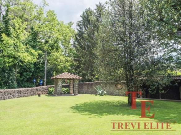 зеленый ухоженный сад с деревьями и лужайкой, уютная беседка с керамической черепичной крышей, каменная стена, спокойная атмосфера, роскошное загородное жилье высокого класса, агентство недвижимости Треви Элит.