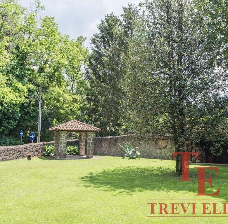 зеленый ухоженный сад с деревьями и лужайкой, уютная беседка с керамической черепичной крышей, каменная стена, спокойная атмосфера, роскошное загородное жилье высокого класса, агентство недвижимости Треви Элит.