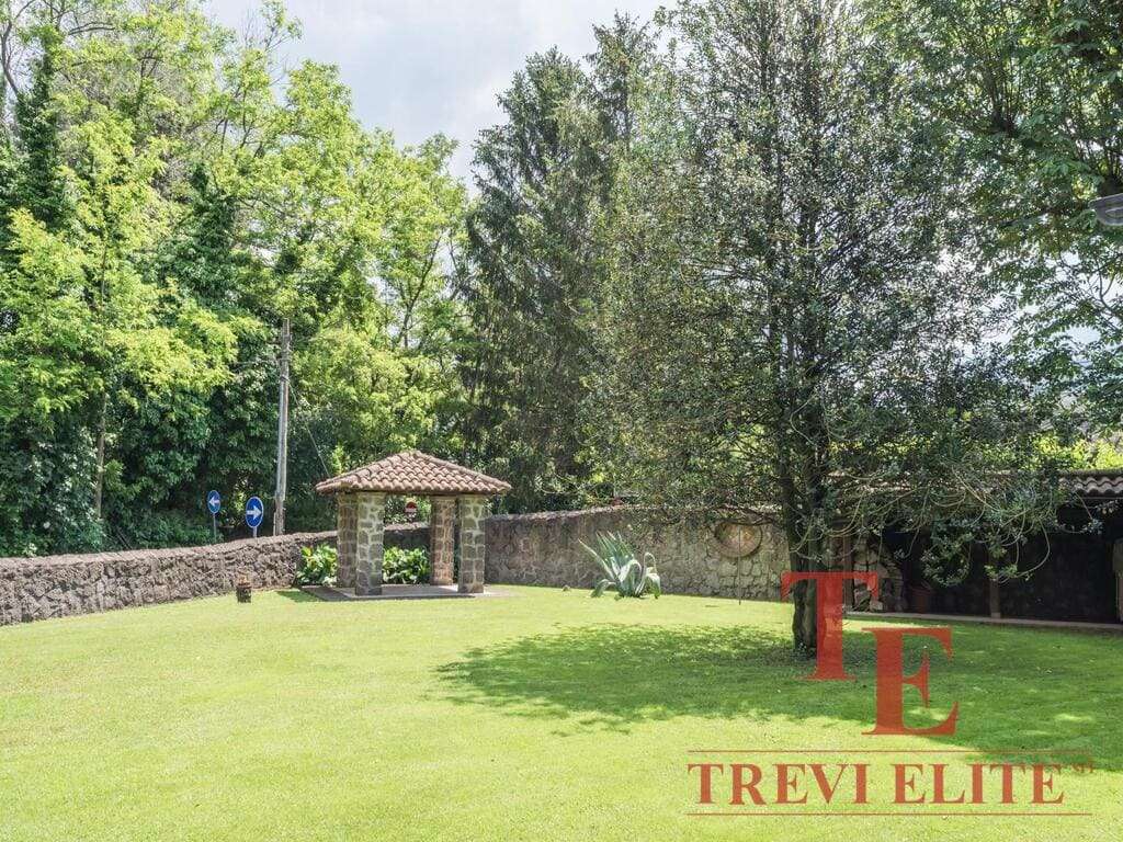 зеленый ухоженный сад с деревьями и лужайкой, уютная беседка с керамической черепичной крышей, каменная стена, спокойная атмосфера, роскошное загородное жилье высокого класса, агентство недвижимости Треви Элит.