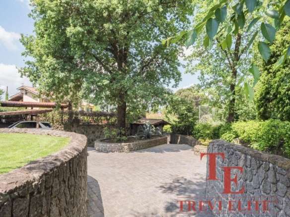 Крупный зеленый дуб, аллея и уютная территория загородного участка с каменными ограждениями и парковкой, предназначенные для элитной недвижимости и эксклюзивных объектов в Италии и по всему миру.