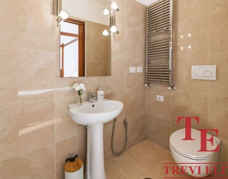 Роскошная современная ванная комната с просторным зеркалом, стилизованной сантехникой и теплым beige-оттенком стен. Идеально оборудована для комфортного проживания.