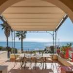 Современная терраса с видом на море и пальмами у элитного итальянского дома. Роскошное пространство для отдыха с уютной тенью и живописным морским пейзажем.