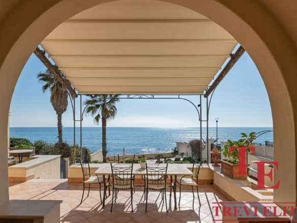 Современная терраса с видом на море и пальмами у элитного итальянского дома. Роскошное пространство для отдыха с уютной тенью и живописным морским пейзажем.