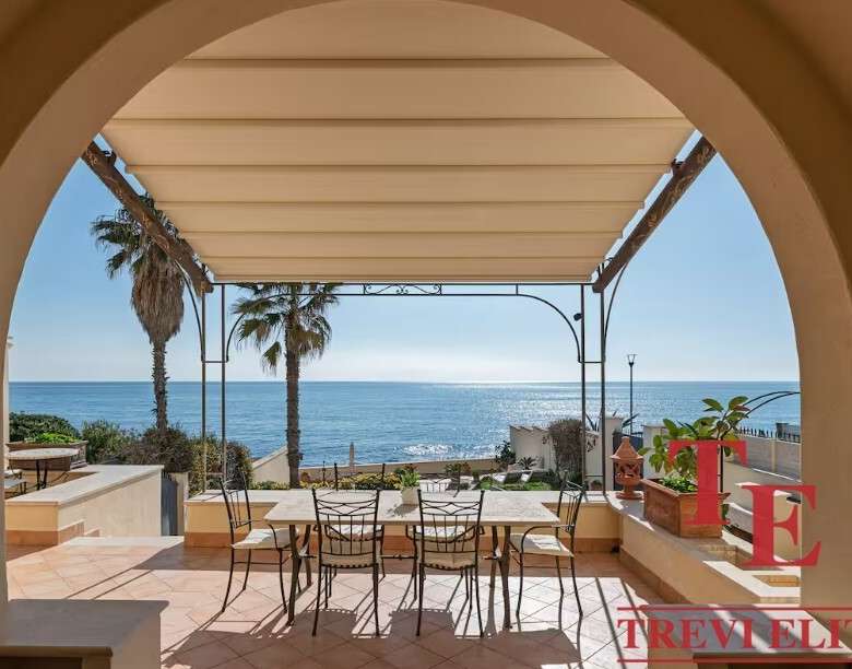 Современная терраса с видом на море и пальмами у элитного итальянского дома. Роскошное пространство для отдыха с уютной тенью и живописным морским пейзажем.