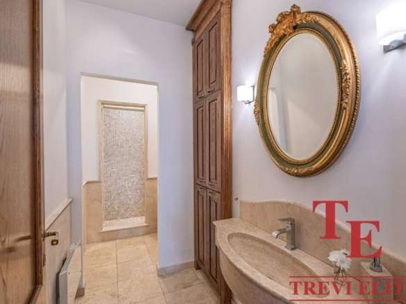 Элегантная ванная комната с классическим зеркалом и деревянными шкафами, выполненная в светлых оттенках, идеально подходит для роскошных интерьеров высокого класса.