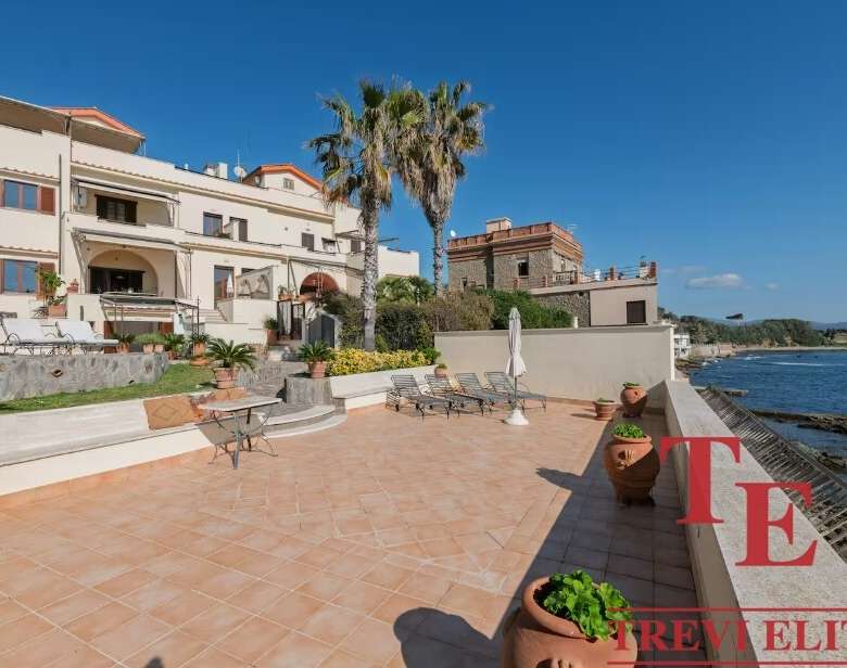 Вид на роскошную виллу у моря с просторной террасой, пальмами и панорамным видом на океан, идеально подходит для элитной недвижимости и роскошных отпуска.