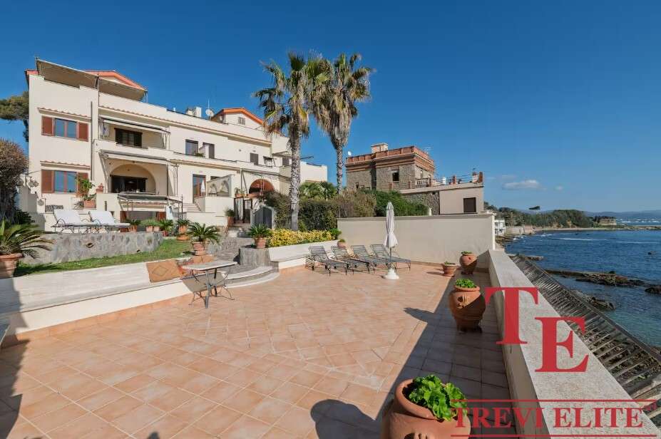 Вид на роскошную виллу у моря с просторной террасой, пальмами и панорамным видом на океан, идеально подходит для элитной недвижимости и роскошных отпуска.