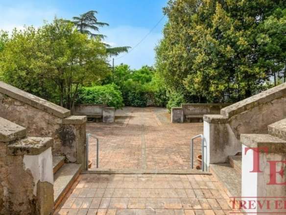 Улица с мощенной дорожкой, окруженная зеленью, с лавками и устойчивой лестницей, создающая уютную атмосферу для отдыха и прогулок на свежем воздухе.