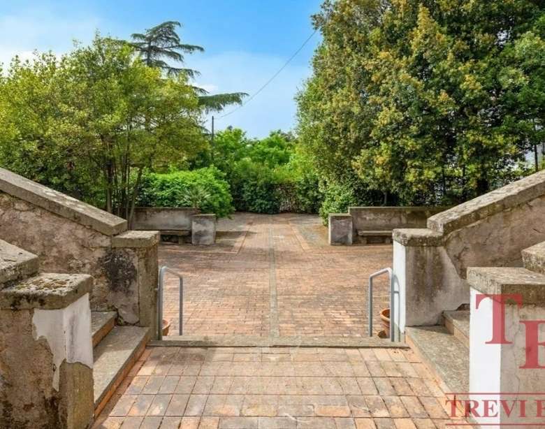 Улица с мощенной дорожкой, окруженная зеленью, с лавками и устойчивой лестницей, создающая уютную атмосферу для отдыха и прогулок на свежем воздухе.