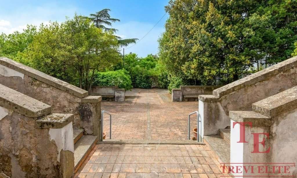 Улица с мощенной дорожкой, окруженная зеленью, с лавками и устойчивой лестницей, создающая уютную атмосферу для отдыха и прогулок на свежем воздухе.