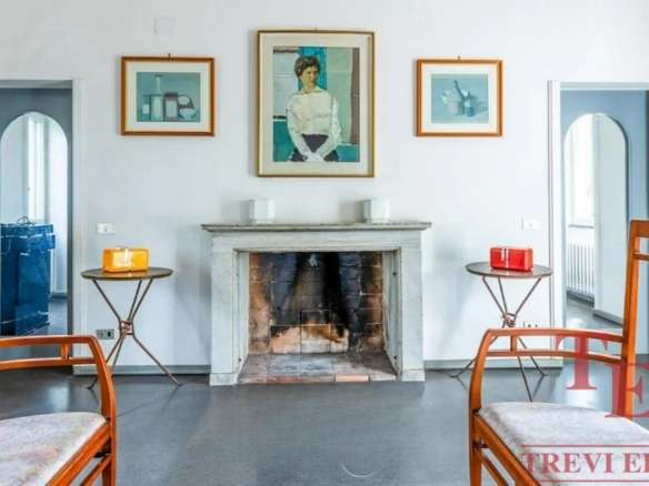 Изысканный интерьер гостиной с камином, картинной галереей и элегантной мебелью, отражающий роскошь и стильность недвижимости высокого класса в Италии и по всему миру.