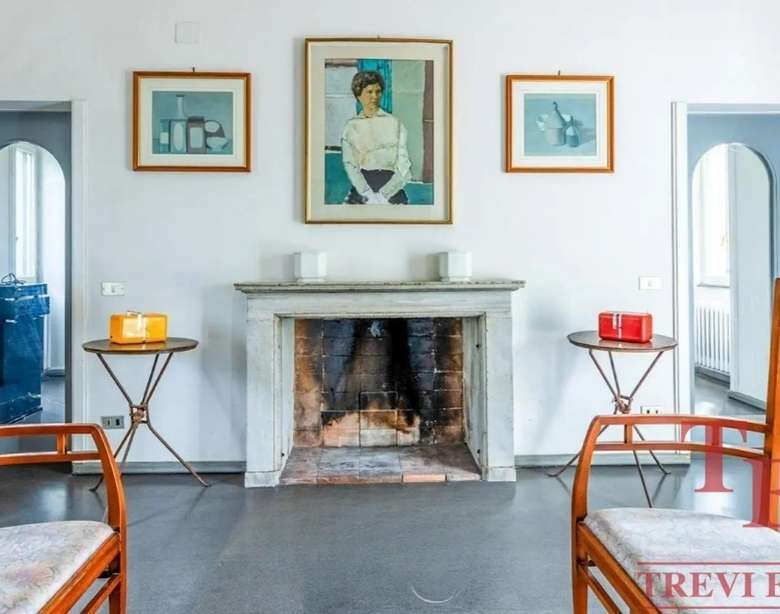 Изысканный интерьер гостиной с камином, картинной галереей и элегантной мебелью, отражающий роскошь и стильность недвижимости высокого класса в Италии и по всему миру.