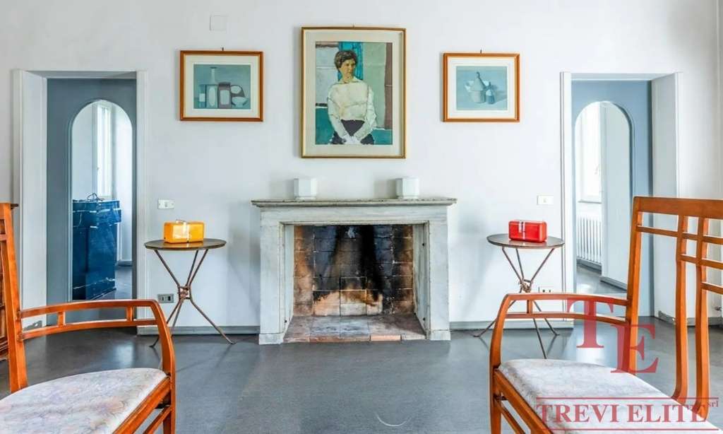 Изысканный интерьер гостиной с камином, картинной галереей и элегантной мебелью, отражающий роскошь и стильность недвижимости высокого класса в Италии и по всему миру.