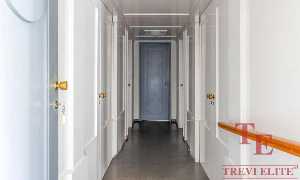 Элегантный коридор в роскошных апартаментах с белыми стенами и золотыми дверными ручками, создающий атмосферу изящества и комфорта в высококлассной недвижимости.