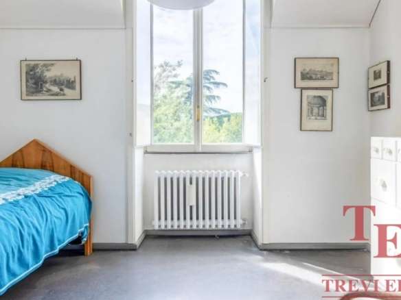 Простая спальня с деревянным кроватью и большим окном, пропускающим естественный свет, в светлом интерьере, подчеркивающем уют и комфорт современного жилья.