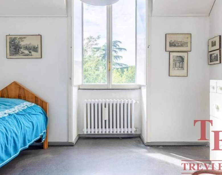 Простая спальня с деревянным кроватью и большим окном, пропускающим естественный свет, в светлом интерьере, подчеркивающем уют и комфорт современного жилья.