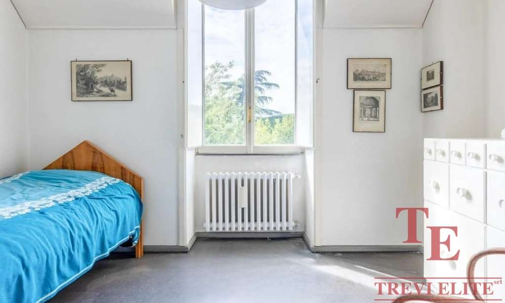 Простая спальня с деревянным кроватью и большим окном, пропускающим естественный свет, в светлом интерьере, подчеркивающем уют и комфорт современного жилья.