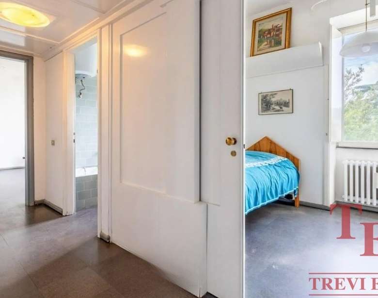 Уютная спальня с большим окном и классической мебелью, яркое естественное освещение, идеально подходит для отдыха и спокойствия. Просторное помещение с радиатором и художественными картинами на стенах.