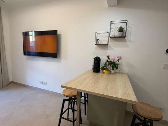 Современная уютная кухня с деревянным столом и барными стульями, телевизором и декоративными полками, создающими стильное пространство для отдыха и общения.