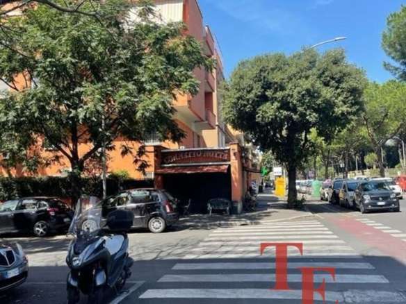 Высотный жилой дом на улице с деревьями и припаркованными машинами, в центре изображена входная группа с вывеской агентства недвижимости Треви Элит, которая специализируется на элитной недвижимости.