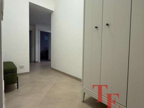 Просторный коридор с белыми стенами и вместительным шкафом, выполненным в светлом цвете, в современном стиле. Идеально подходит для хранения одежды и аксессуаров в элитной квартире.