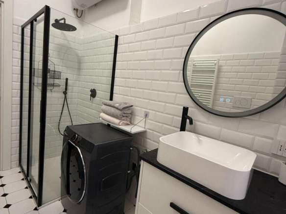 Современная ванная комната с душевой кабиной, раковиной в стиле лофт, стиральной машиной и элементами черного и белого дизайна. Идеально подходит для роскошного жилого пространства.