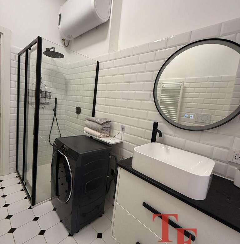 Современная ванная комната с душевой кабиной, раковиной в стиле лофт, стиральной машиной и элементами черного и белого дизайна. Идеально подходит для роскошного жилого пространства.