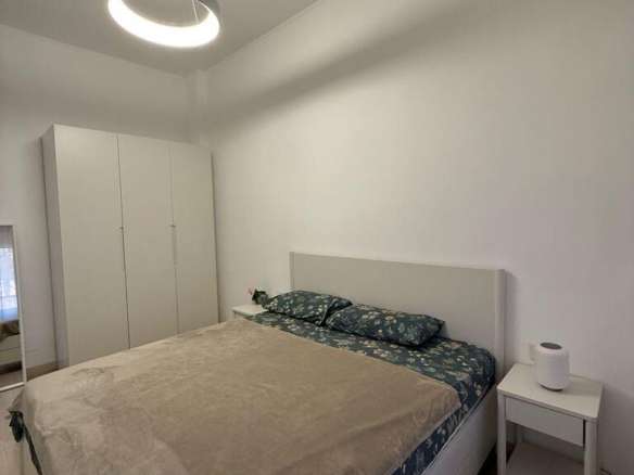 Минималистичная спальня в элитной недвижимости с белыми стенами, удобной кроватью с красивой постелью и светильником современного дизайна, выполнена в стиле роскошного жилья.