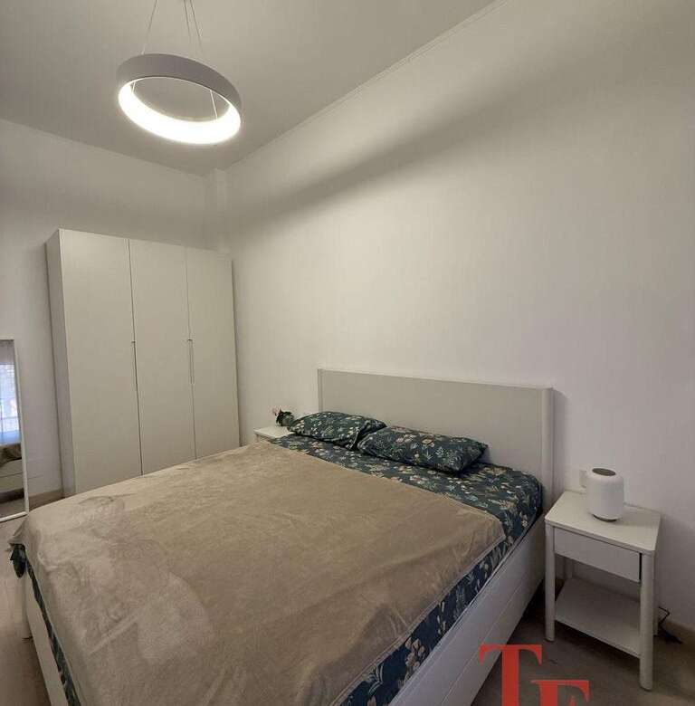 Минималистичная спальня в элитной недвижимости с белыми стенами, удобной кроватью с красивой постелью и светильником современного дизайна, выполнена в стиле роскошного жилья.