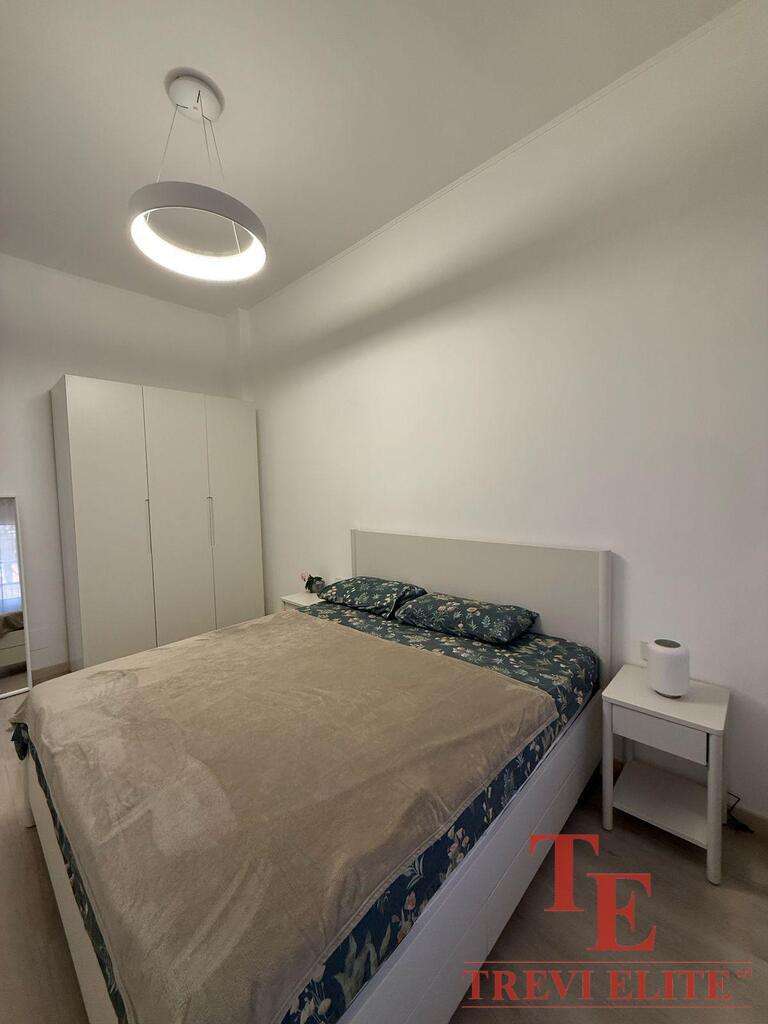 Минималистичная спальня в элитной недвижимости с белыми стенами, удобной кроватью с красивой постелью и светильником современного дизайна, выполнена в стиле роскошного жилья.