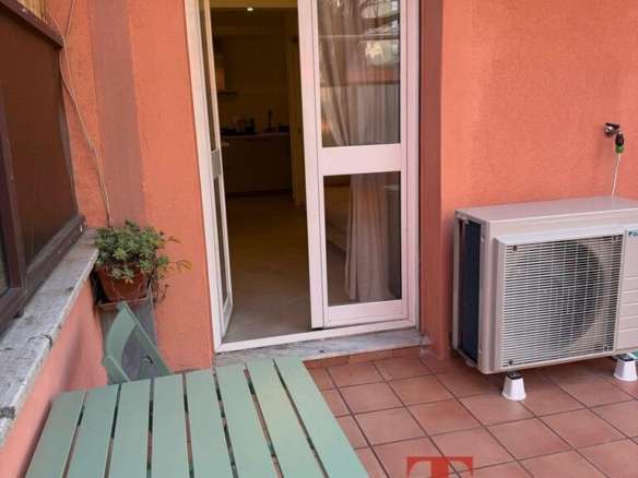 Современный балкон с уютной мебелью, выходящий на жилой дом с окнами, обеспечивающими естественное освещение и панорамный вид. Идеальное место для отдыха и наслаждения видом на город.