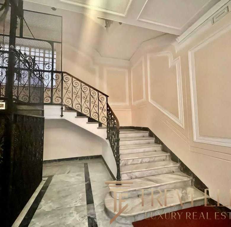 Элегантный интерьер лестничной клетки в роскошном здании с мраморными ступенями и декоративными панелями. Изысканный дизайн и стильный кованый балясина подчеркивают высокое качество недвижимости.