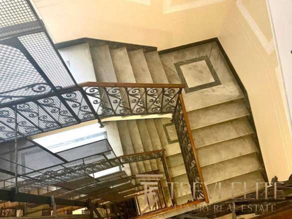 Изящная лестница с кованым балюстраном и мраморными ступенями, ведущая на верхний этаж роскошного жилья, создающая элегантную атмосферу и подчёркивающая высокий статус недвижимости.