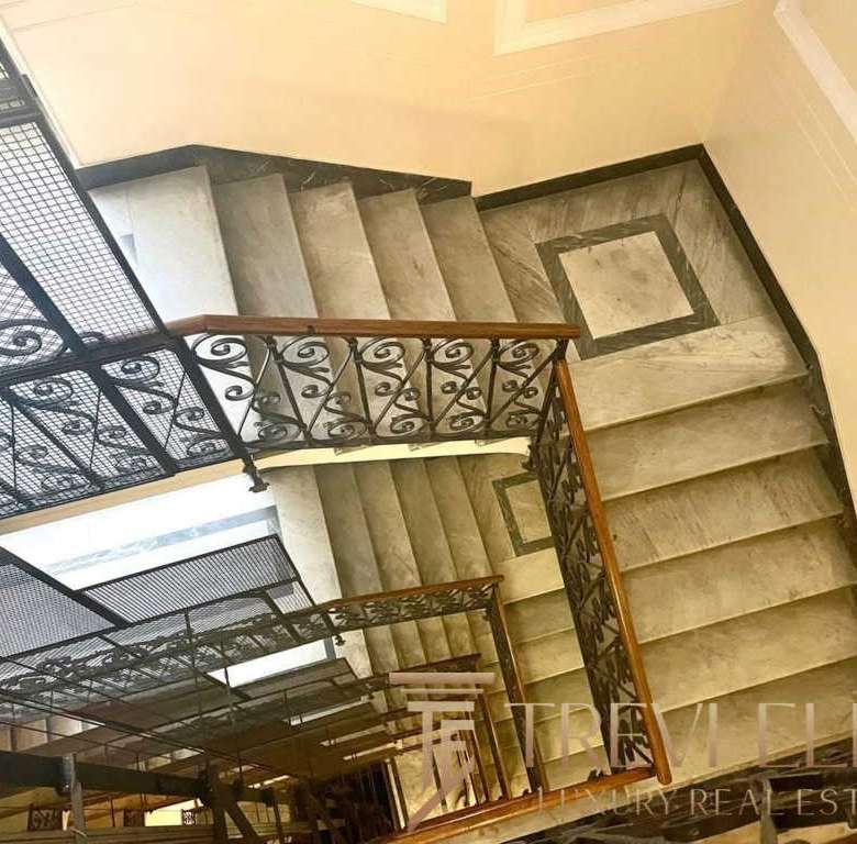 Изящная лестница с кованым балюстраном и мраморными ступенями, ведущая на верхний этаж роскошного жилья, создающая элегантную атмосферу и подчёркивающая высокий статус недвижимости.