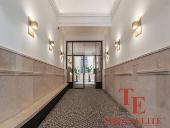 Элегантный коридор в офисном здании с современным дизайном, белыми стенами, множеством светильников и стеклянной дверью, ведущей на прогулочный балкон, создавая атмосферу роскоши и стиля.